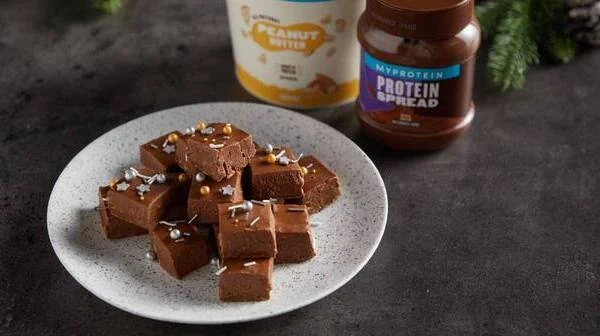 Pieces of chocolate protein spread and peanut butter fudge with edible Christmas decorations on top